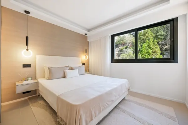 Chambre lumineuse aux boiseries claires avec grande fenêtre sur la verdure, dans un appartement 3 pièces rénové du Mont-Boron