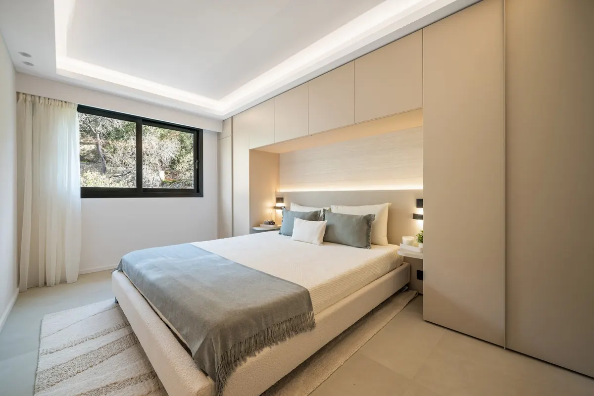 Camera con letto matrimoniale, coperta grigia e blu, testata rivestita in legno e grande finestra sul verde