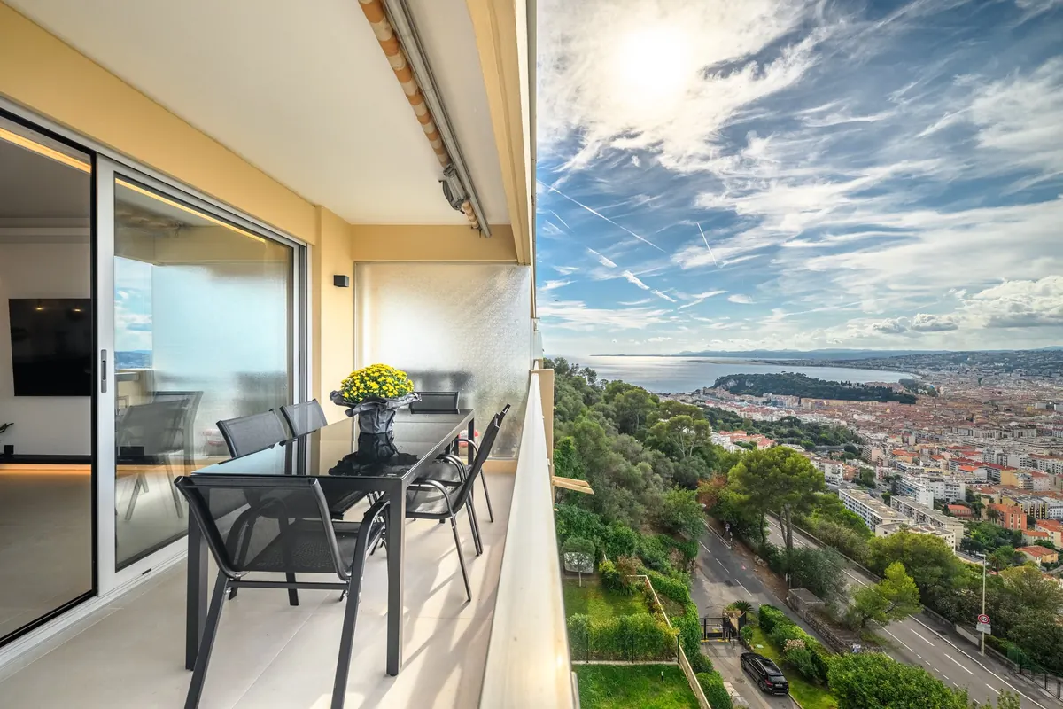 Terrazza dell'appartamento con tavolo e sedie e vista sulle colline boscose e sul litorale nizzardo